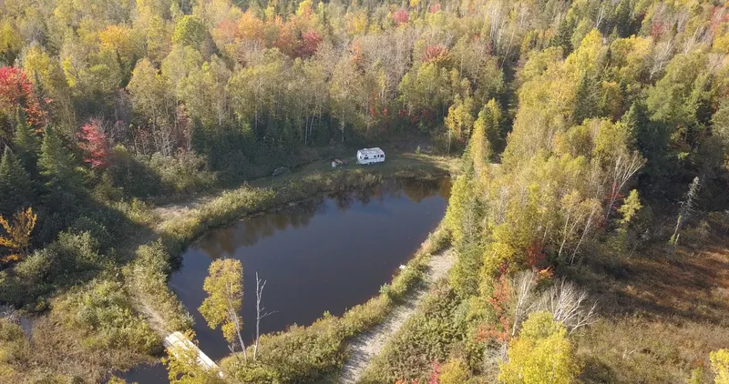 Vue de drone d’un lac privé entouré d’une forêt aux couleurs d’automne, sur un domaine de 42 acres