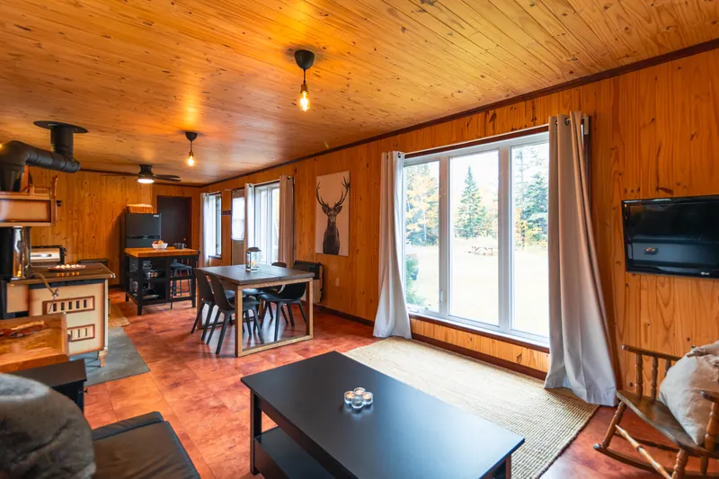 Salon lumineux tout en bois de pin, avec une grande fenêtre et la cuisine au fond