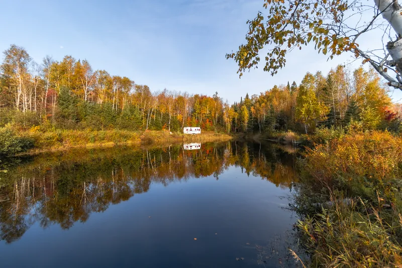 Lac privé bordé d’arbres d’automne qui se reflètent dans l’eau calme, sous un ciel bleu