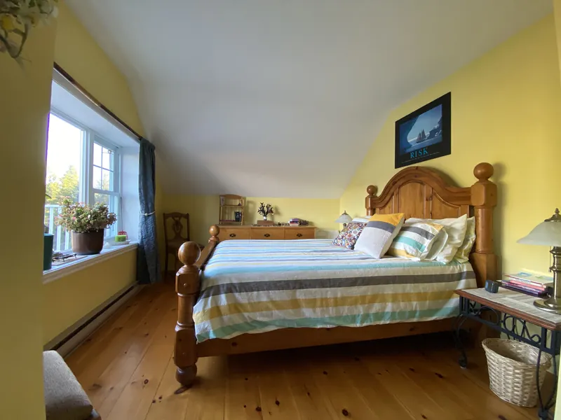 Chambre aux murs jaunes et plafond en pente, avec un lit en pin et une fenêtre lumineuse