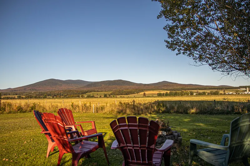 Chaises Adirondack rouges sur le terrain, face aux champs et aux montagnes