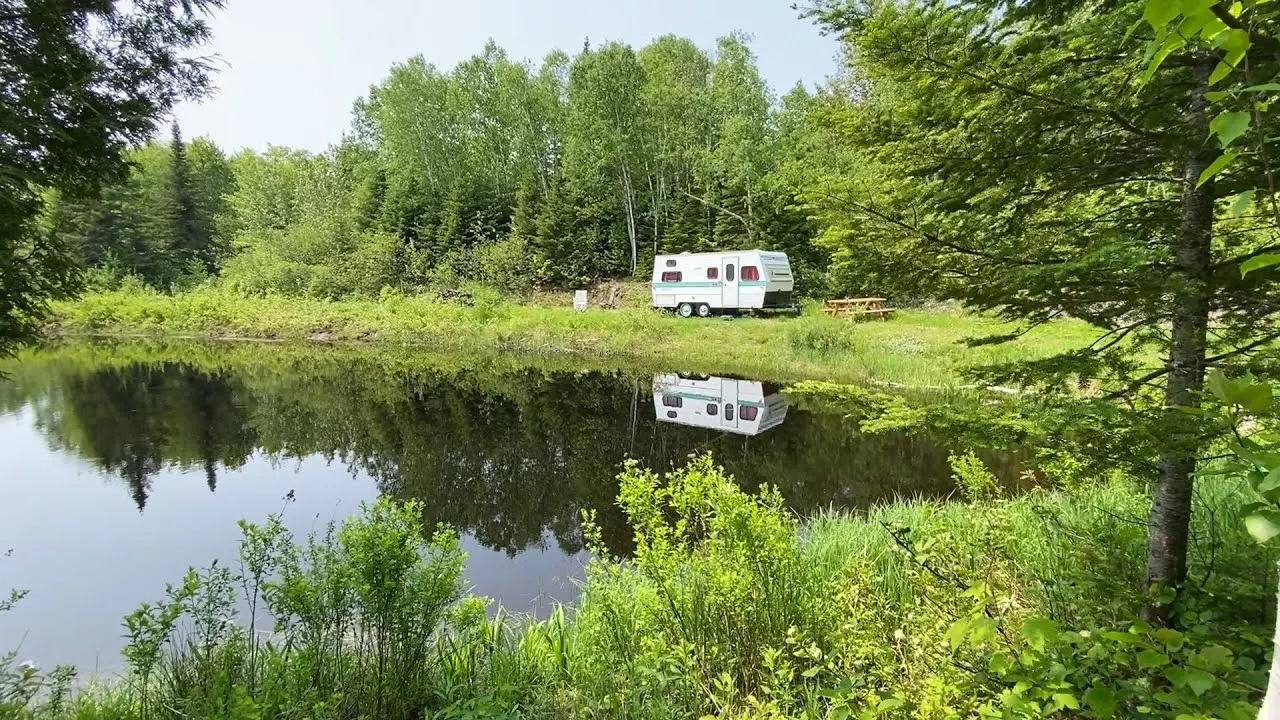 Un lac calme bordé de forêt, une roulotte et une table de pique-nique sur la rive